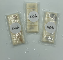Load image into Gallery viewer, The picture is of a wax melt in the shape of a chocolate bar. The colour is white with gold and silver biodegradable glitter wrapped in plastic with the brand name "Kotcha" on it. There are crystals surrounding the image and a white background.
