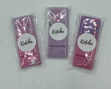 Load image into Gallery viewer, The picture is of a wax melt in the shape of a chocolate bar. The colour is purple with silver biodegradable glitter wrapped in plastic with the brand name "Kotcha" on it. There are crystals surrounding the image and a white background.
